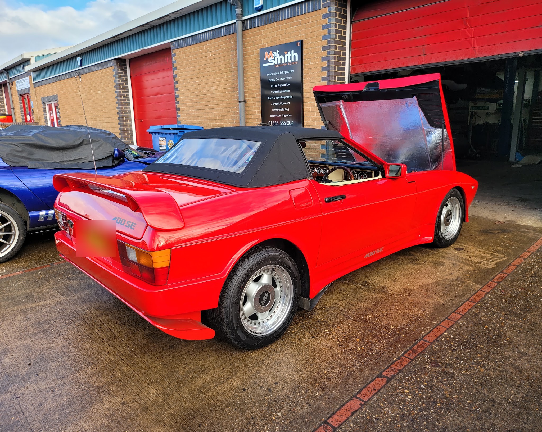 A red TVR wedge outside the workshop with the services sign on the wall behind